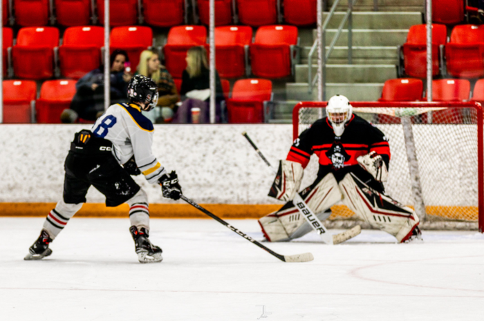 student hockey player taking a shot on a teacher goalie