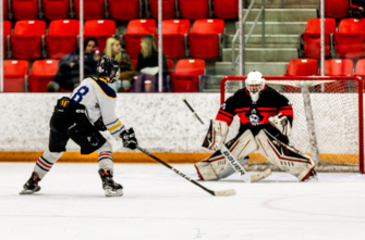 student hockey player taking a shot on a teacher goalie