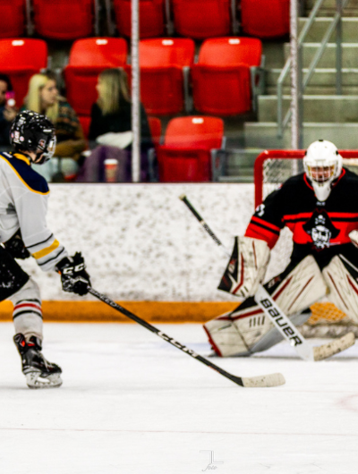 Student hockey player shooting the puck on a staff goalie